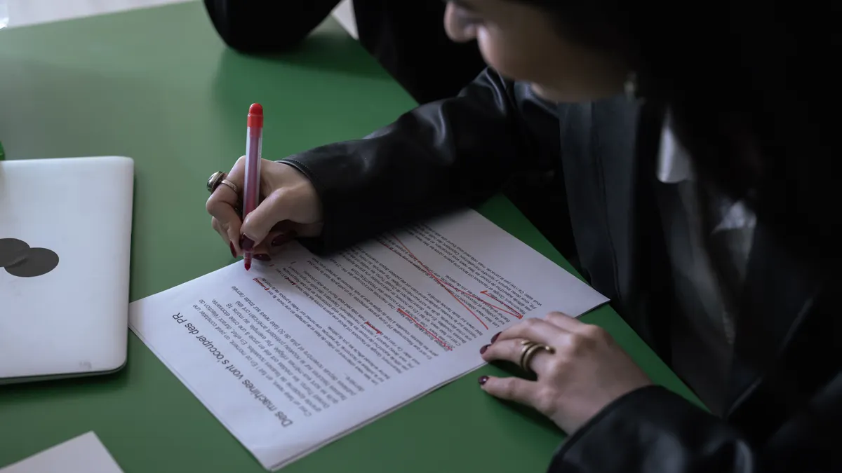 Person reviewing and marking up a document beside a laptop